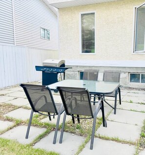 Eine Außenpatio mit Tisch, Stühlen, einem Grill und einem Haus im Hintergrund.