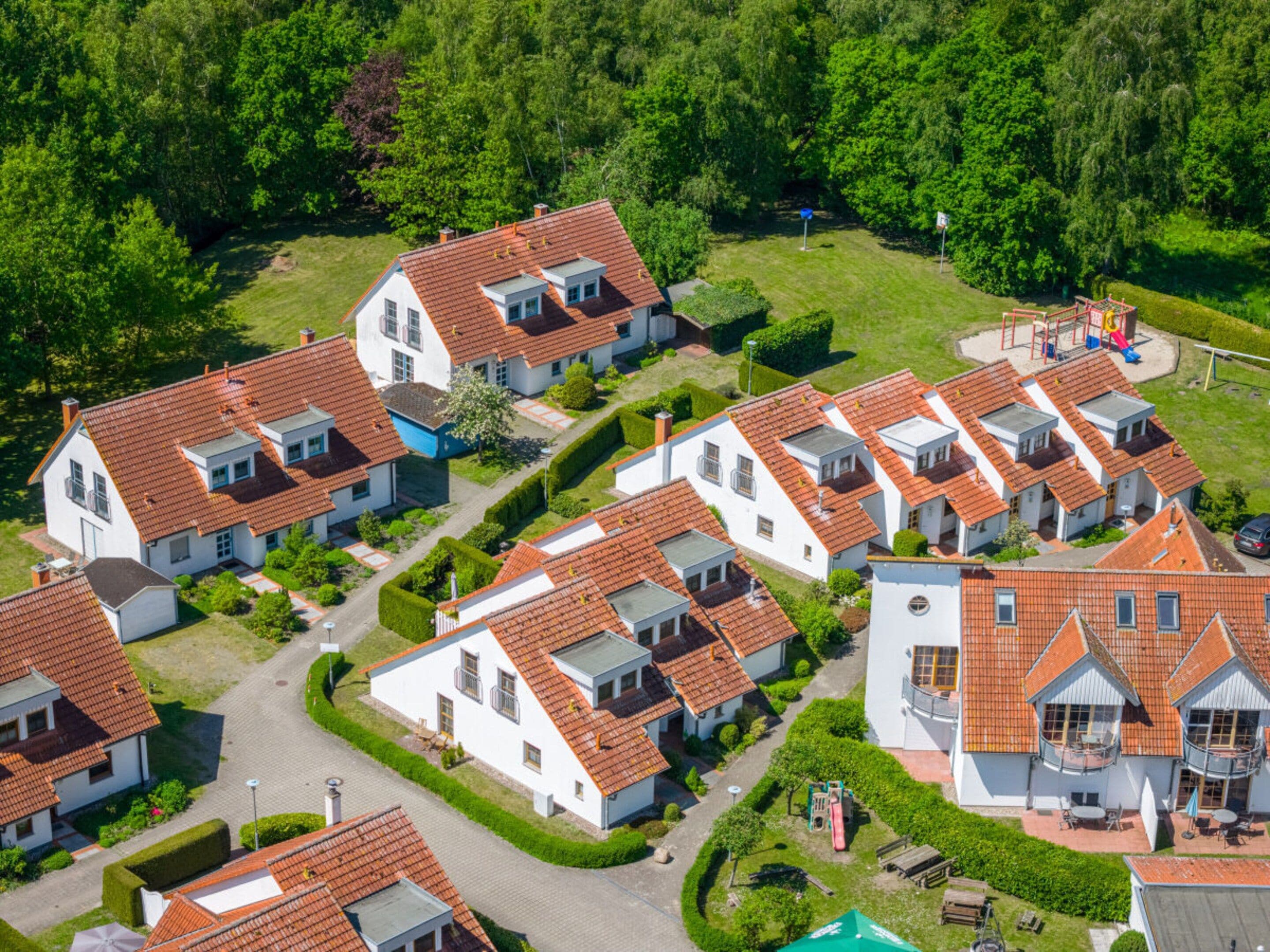 Un quartier résidentiel composé de plusieurs maisons aux toits recouverts de tuiles rouges et aux murs blancs, le tout entouré d’une végétation luxuriante.