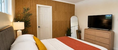 Hotellihuone, jossa on sänky, kattotuuletin, televisio, lipasto ja ovi.