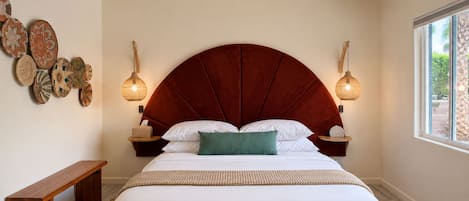 A bedroom with a large bed, a ceiling fan, wall-mounted lamps, and a bench.