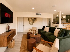 A living room with a flat-screen TV, a green sofa, a wooden coffee table, and a wooden bench. - Wellness Retreat: Pool, Hot Tub, Mini Golf, Outdoor Shower + Old Town Scottsdale (Scottsdale)