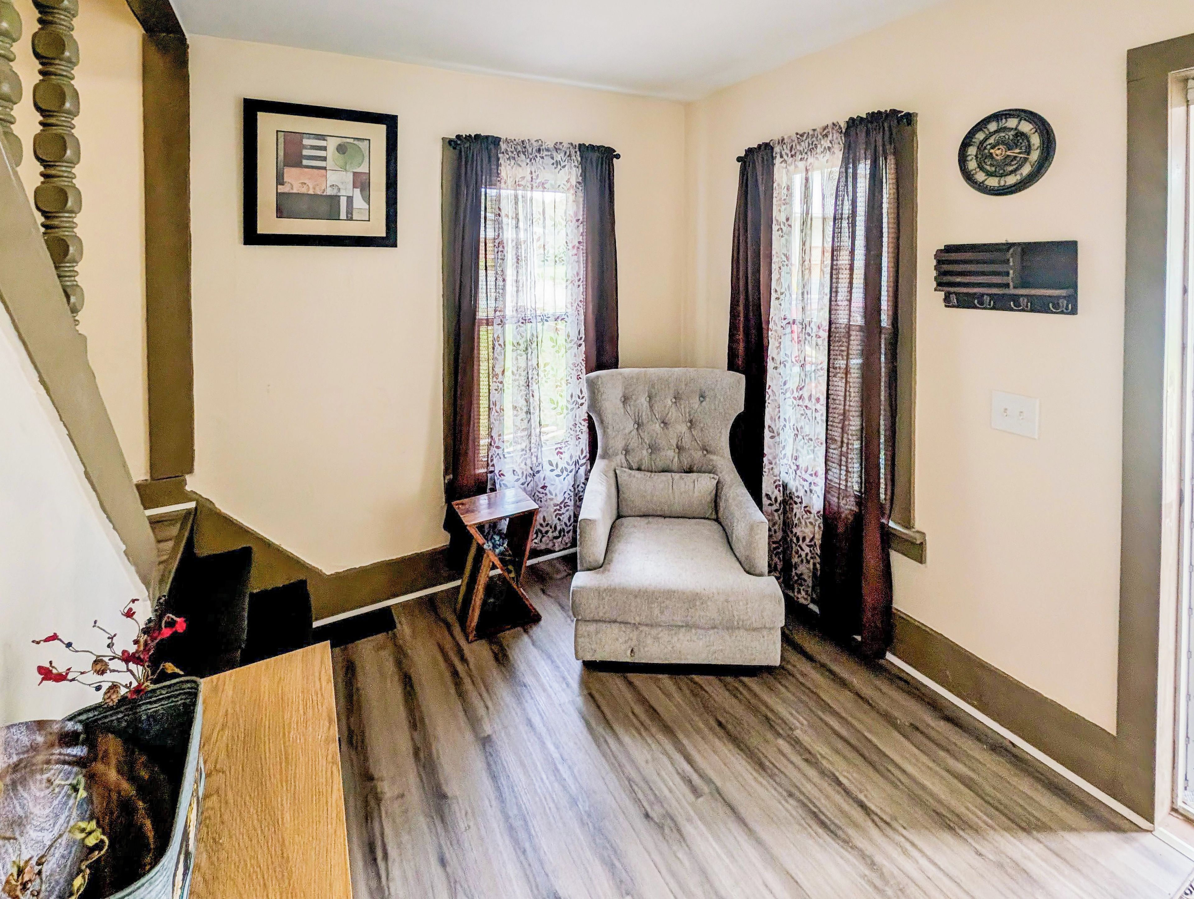 A room with a wooden floor, a chair, a framed picture on the wall, and a clock.