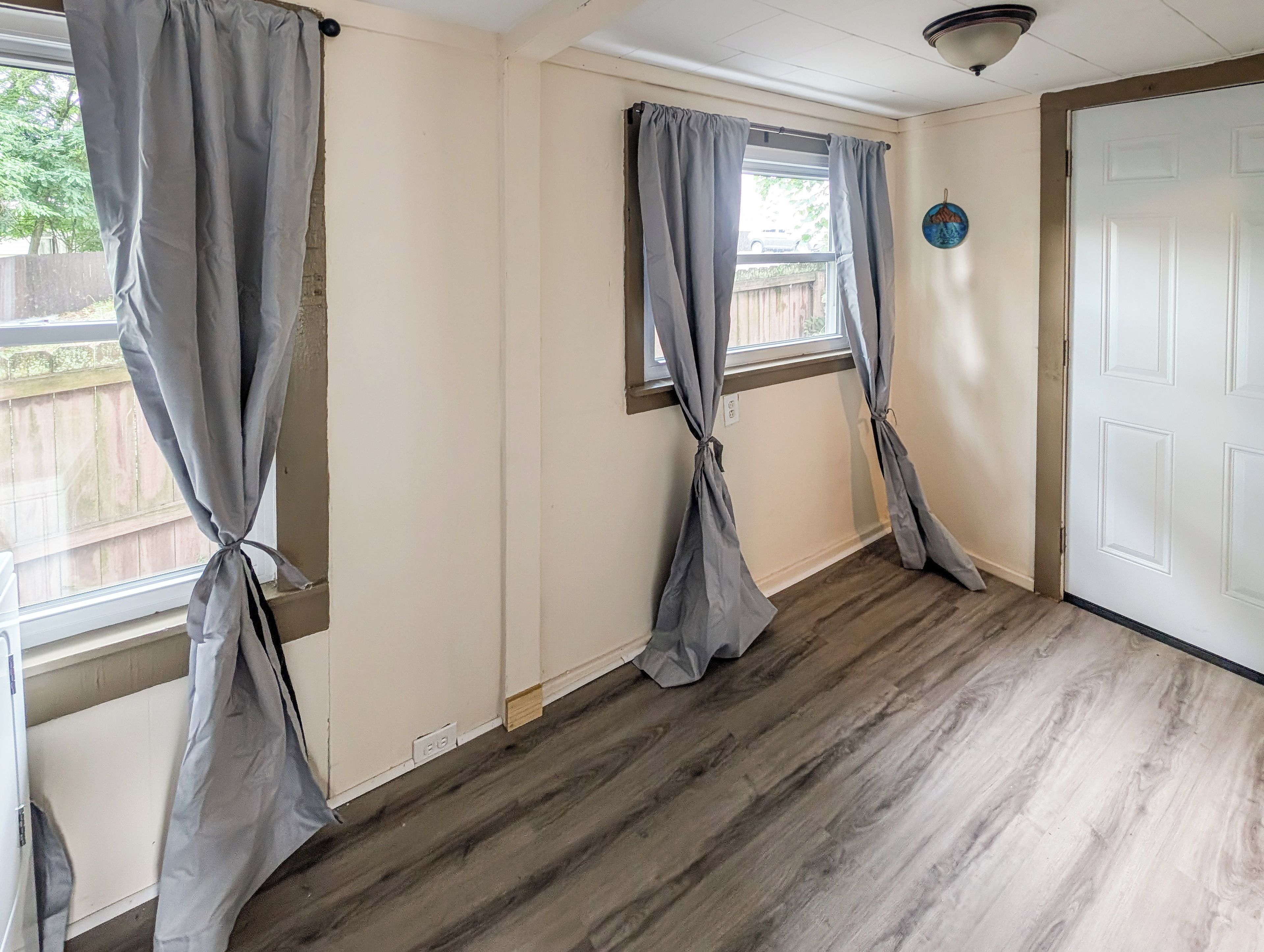 A room with two windows, wooden flooring, and a white door.