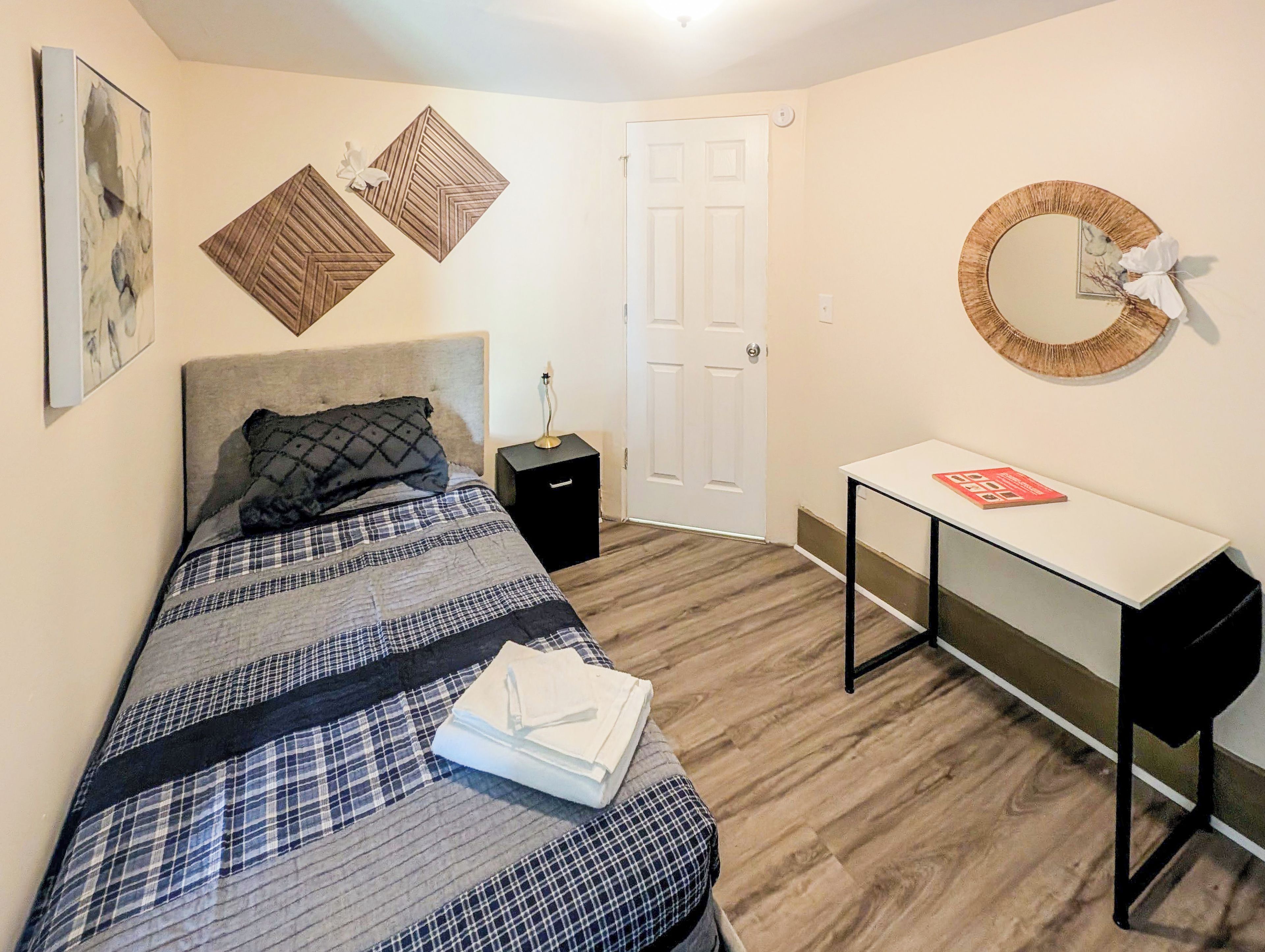 A bedroom with a bed, bedside table, desk, and a door.