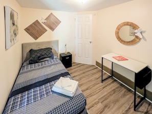 A bedroom with a bed, bedside table, desk, and a door.