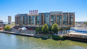 Un hotel frente al agua con un diseño arquitectónico moderno, que presenta un cartel llamativo de Flats East Bank, una zona de embarque y un restaurante llamado Lake House.