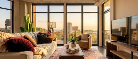 A modern living room with a large window, a sofa, a coffee table, and a TV.