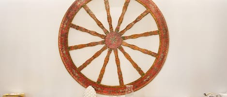 A wall-mounted decorative wheel with a rustic design, a stone wall, and a buffet setup with plates, glasses, and a pitcher.