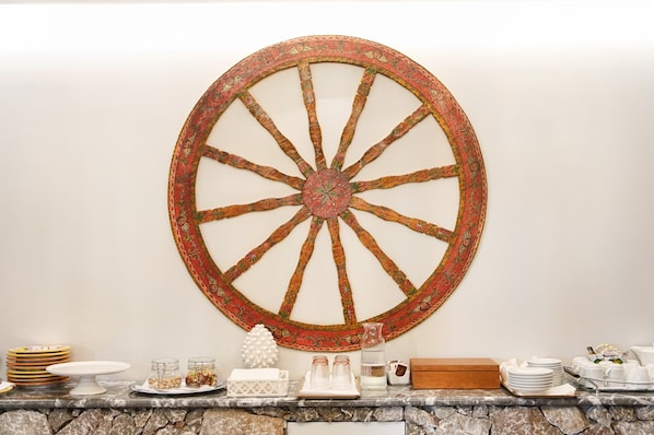 A wall-mounted decorative wheel with a rustic design, a stone wall, and a buffet setup with plates, glasses, and a pitcher.