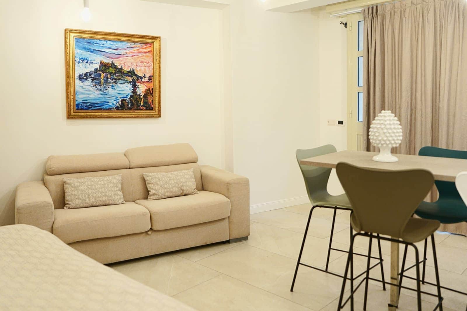 Una sala de estar con un sofá color beige, una mesa de comedor con sillas y un cuadro en la pared.