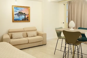 A living room with a beige sofa, a dining table with chairs, and a painting on the wall.