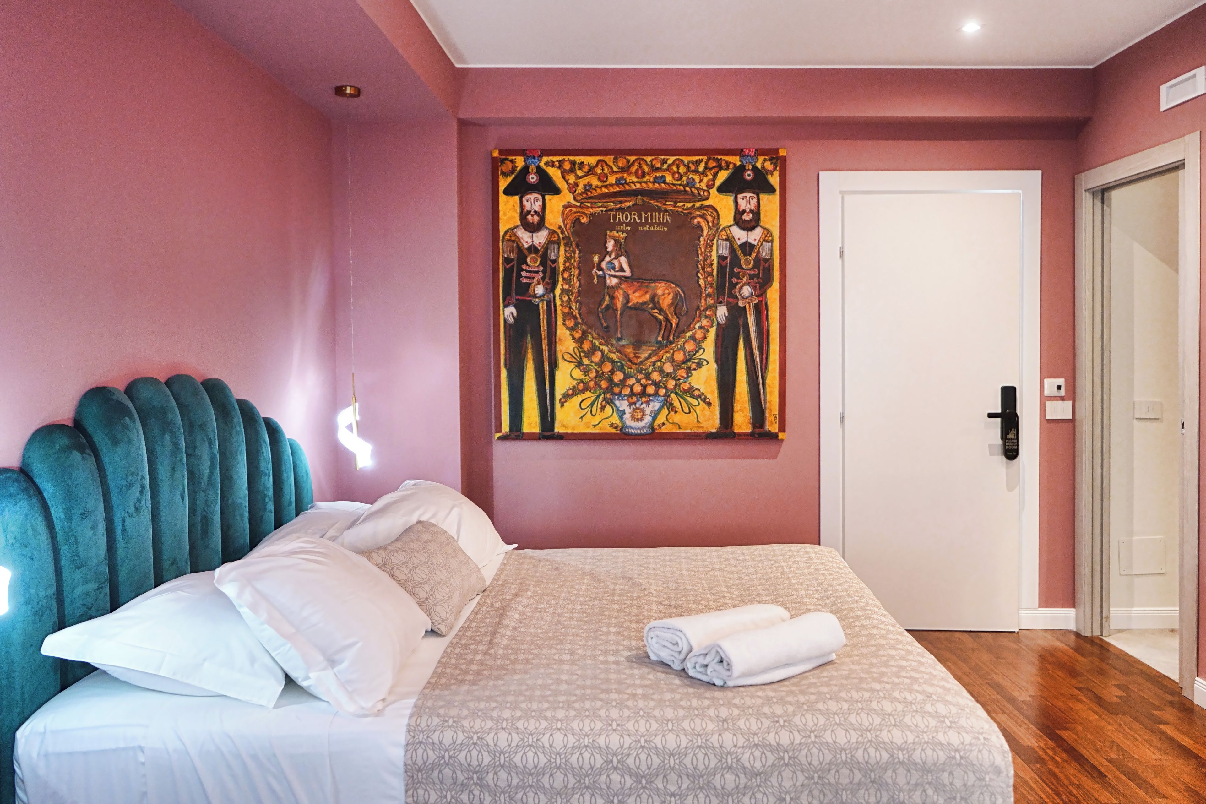 A bedroom with a bed, pillows, a headboard, a painting, and a door.