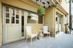 A building facade with a large window, a hanging plant, and a small table with a chair.