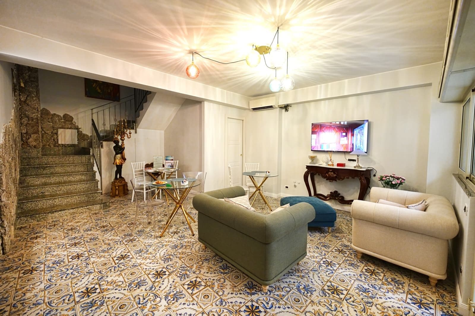 A living room with a patterned floor, a staircase, a television, and a statue.