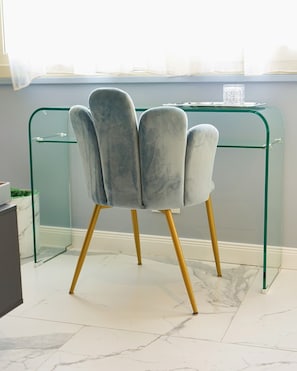 A chair with a unique design, positioned in front of a glass desk with a metal frame.