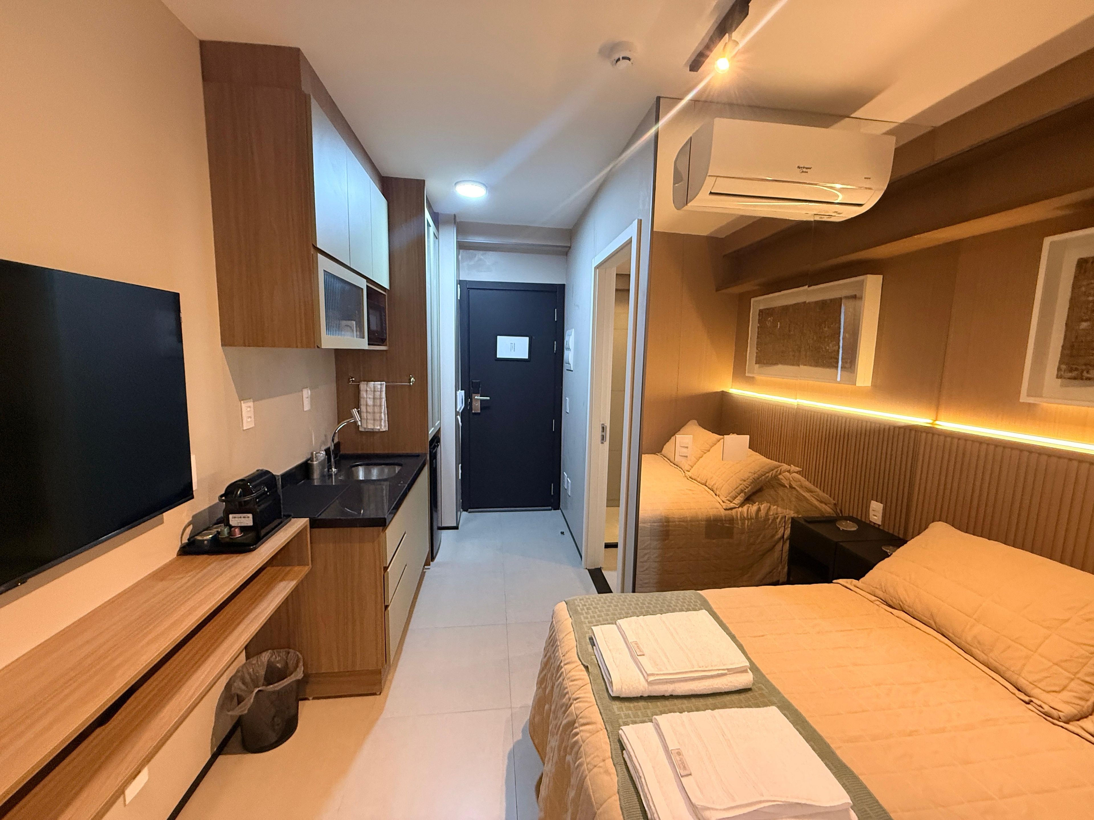 Une chambre d’hôtel de taille réduite, comprenant un lit, une télévision, une kitchenette et une salle de bain.