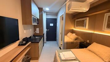 Une chambre d’hôtel de taille réduite, comprenant un lit, une télévision, une kitchenette et une salle de bain.