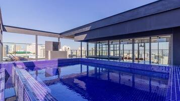 Une piscine sur le toit offrant une vue sur la ville, entourée de murs de verre et dotée d’une architecture moderne.