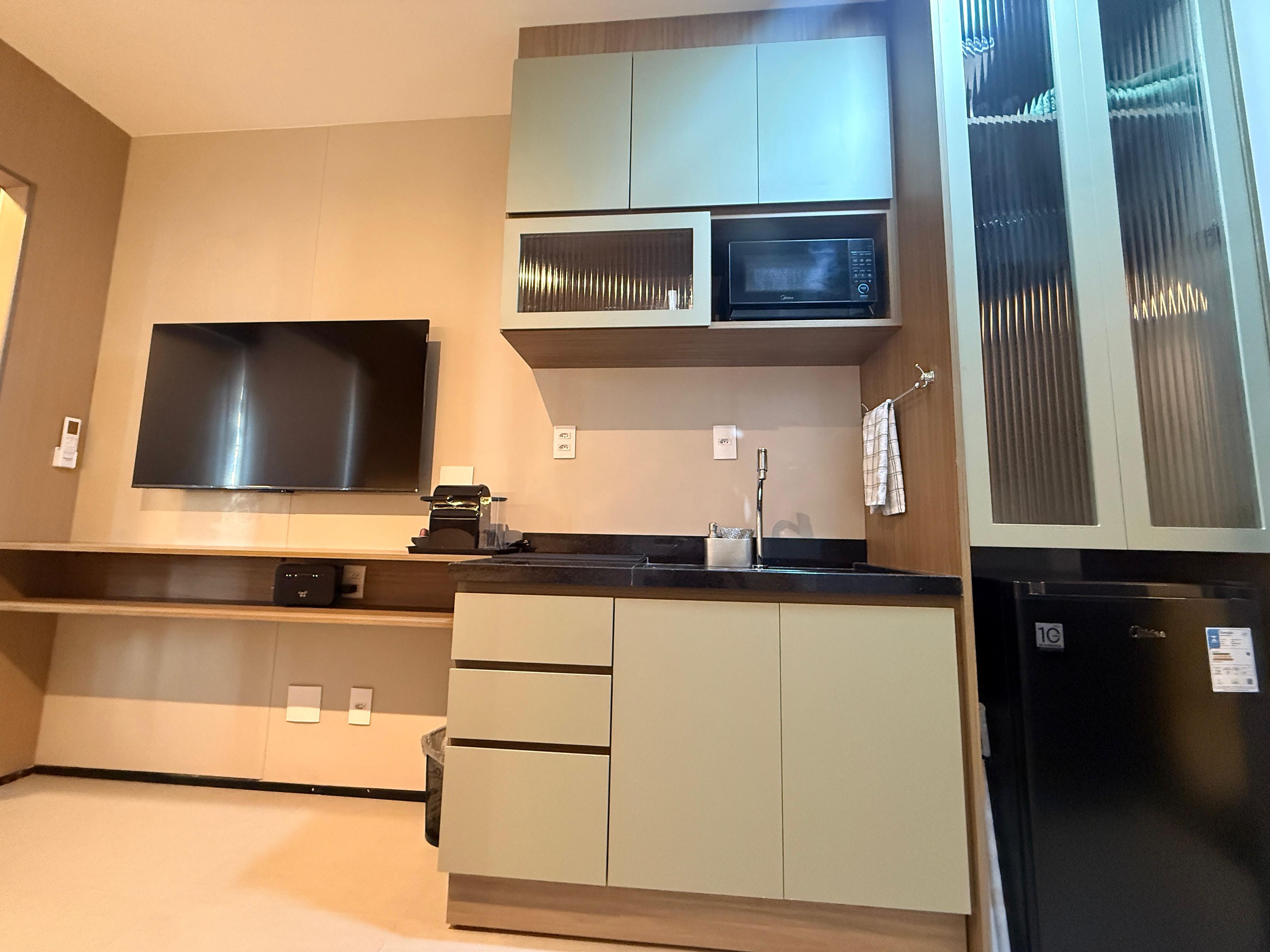Cozinha moderna com televisão de tela plana, micro-ondas e geladeira.