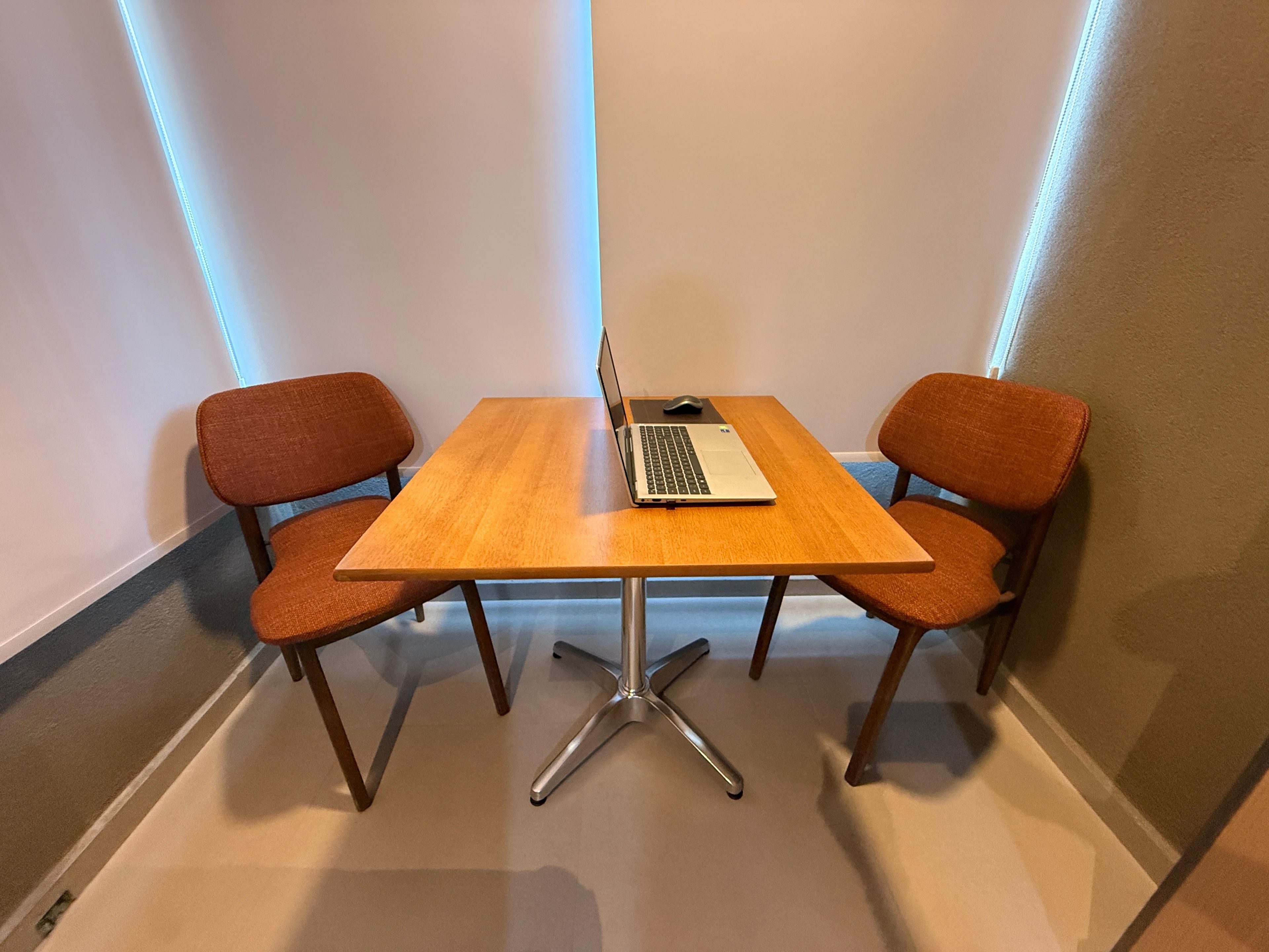 Pequena sala de reuniões com uma mesa de madeira, duas cadeiras e um laptop.