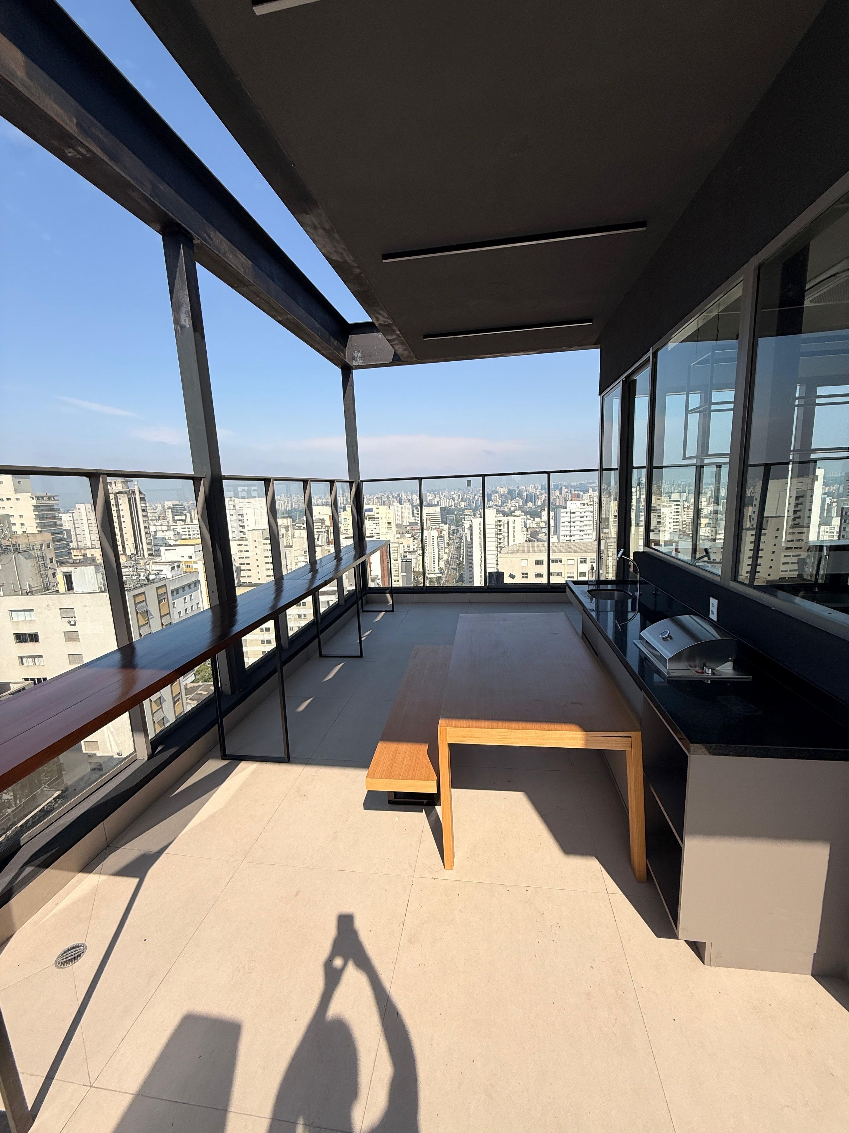 Un balcon situé dans un immeuble de grande hauteur, offrant une vue sur le paysage urbain, avec un banc en bois et une petite table sur laquelle se trouve une tasse.