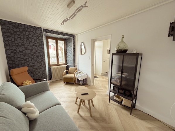 A living room with a sofa, a small round table, a cabinet with speakers, and a radiator. - Holiday Home 'Étape À Monestier Du Percy' with Mountain View and Private Terrace (Monestier-du-Percy)