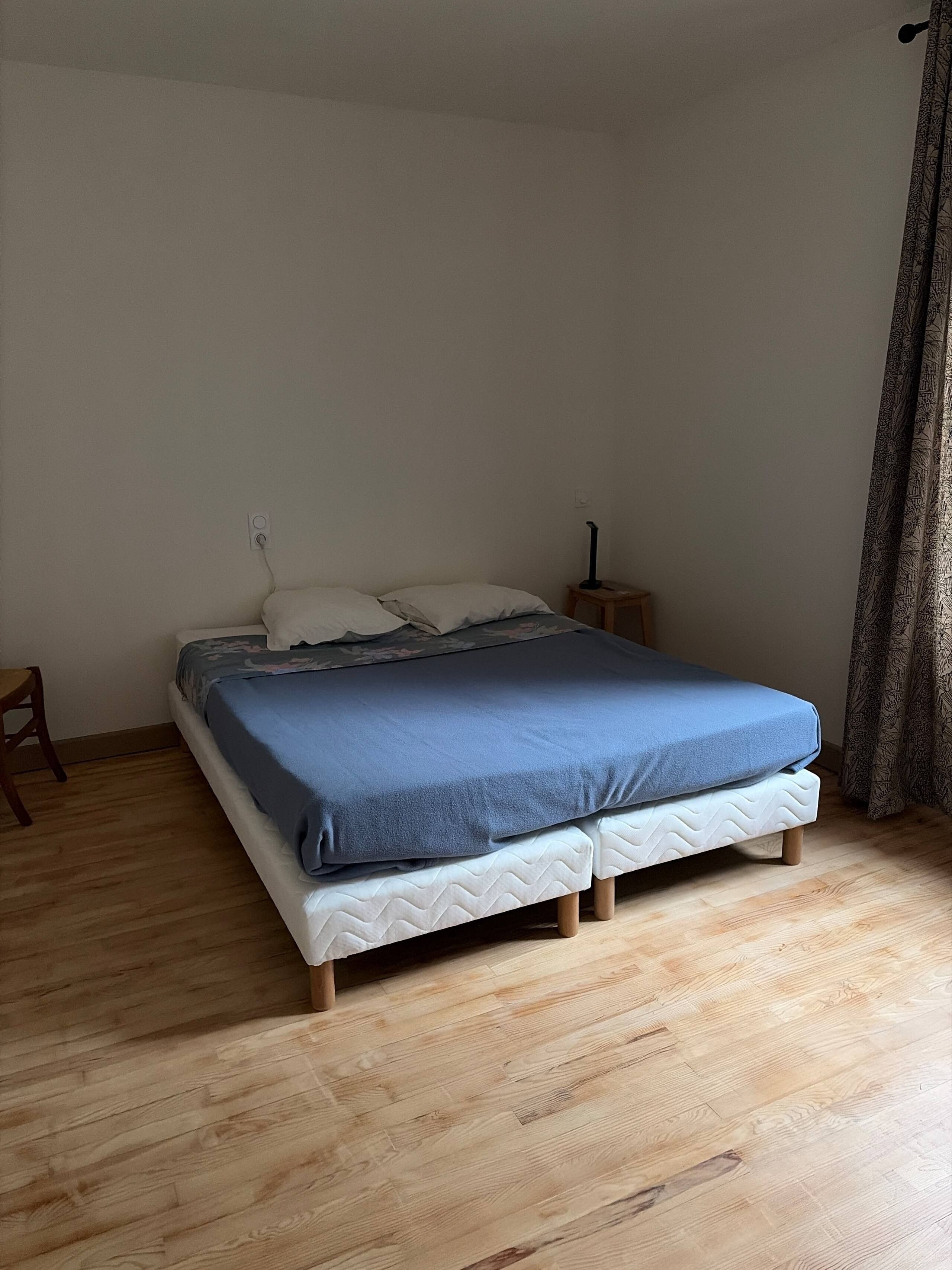 Een eenpersoonsbed met een blauwe deken, een nachtkastje en een lamp.