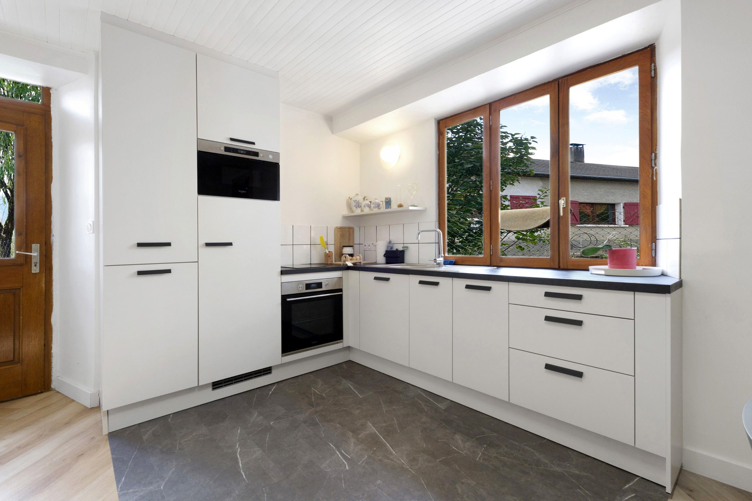 Une cuisine moderne avec des meubles blancs, un four encastré et une fenêtre donnant sur l’extérieur.