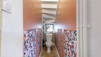 Een smalle gang met behang met patroon, een witte deur aan de rechterkant, en een toilet in de verte.