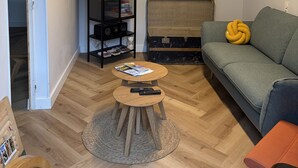 A living room with a sofa, a coffee table, a television mounted on the wall, a bookshelf, and a trunk. - Holiday Home 'Étape À Monestier Du Percy' with Mountain View and Private Terrace (Monestier-du-Percy)