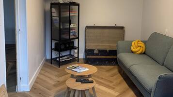 Een woonkamer met een bank, een salontafel, een aan de muur bevestigde televisie, een boekenkast en een koffer.