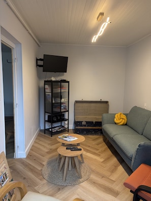 A living room with a sofa, a coffee table, a television mounted on the wall, a bookshelf, and a trunk. - Holiday Home 'Étape À Monestier Du Percy' with Mountain View and Private Terrace (Monestier-du-Percy)