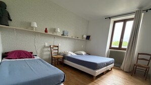 A room with two beds, a chair, a shelf with books and a lamp, and a window with curtains. - Holiday Home 'Étape À Monestier Du Percy' with Mountain View and Private Terrace (Monestier-du-Percy)