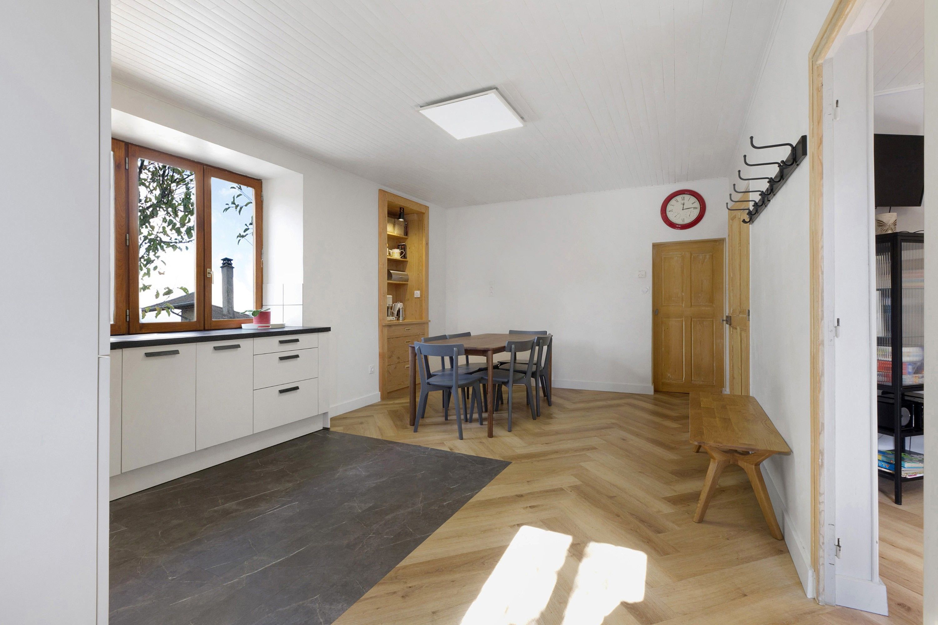 A compact kitchen with a dining area, wooden cabinets, a built-in shelf, and a clock on the wall.