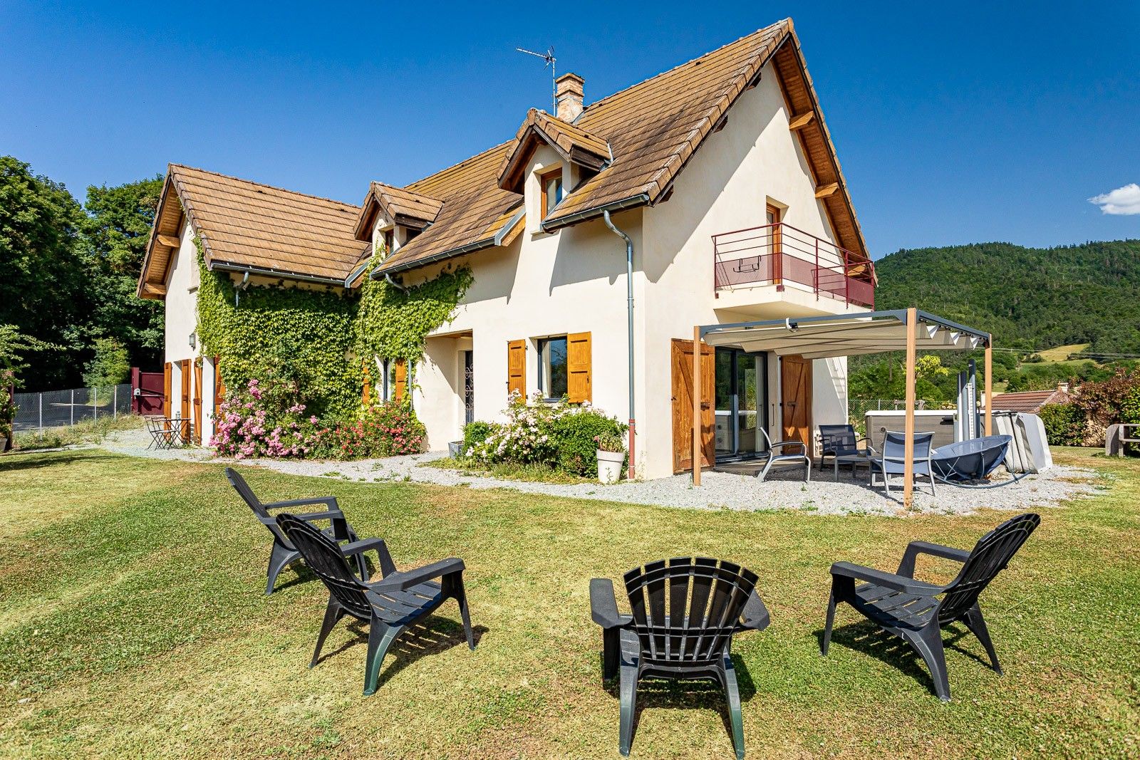 Ein zweistöckiges Haus mit überdachter Terrasse, Sitzgelegenheiten im Freien und einem Garten.