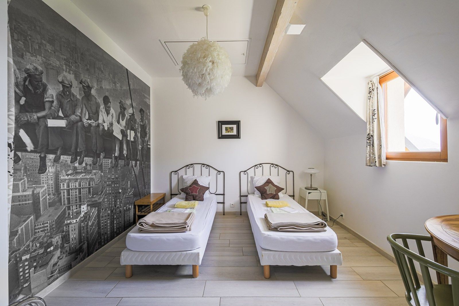 A room with two beds, a large mural, a hanging light fixture, and a skylight.