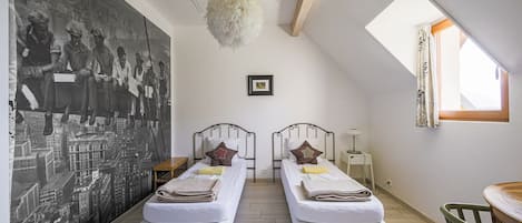 A room with two beds, a large mural, a hanging light fixture, and a skylight.
