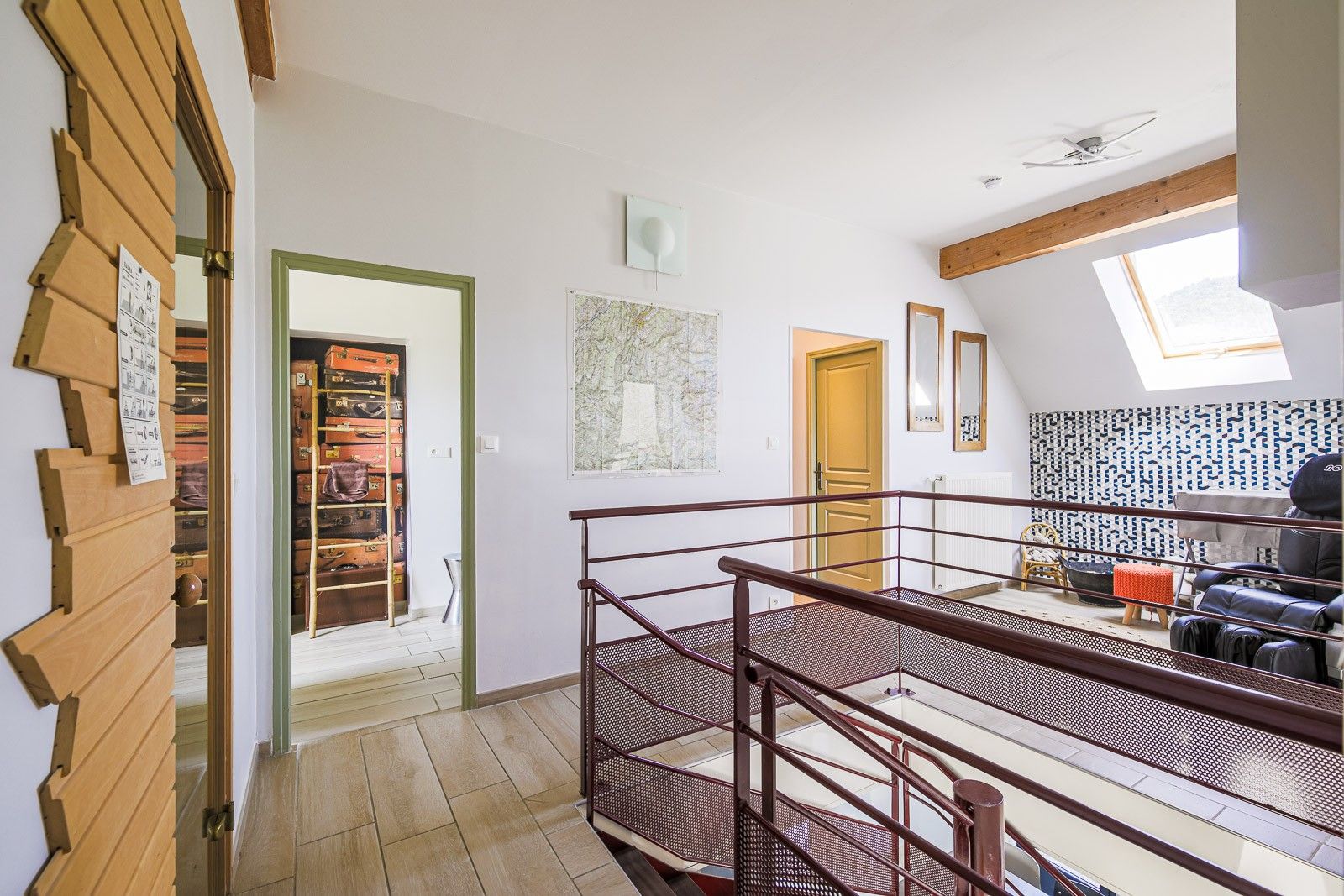 A spacious loft with a high ceiling, a wooden staircase, a seating area with a sofa and armchairs, and a collection of luggage on shelves.