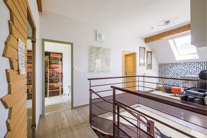 Een ruime loft met een hoge plafond, een houten trap, een zithoek met een bank en fauteuils, en een verzameling bagage op planken.