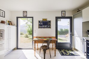 A kitchen with a view of the outdoors, a wooden table, and a chair. - Holiday Home 'La Bayloune' with Mountain View, Private Terrace and Wi-Fi (Lavars)