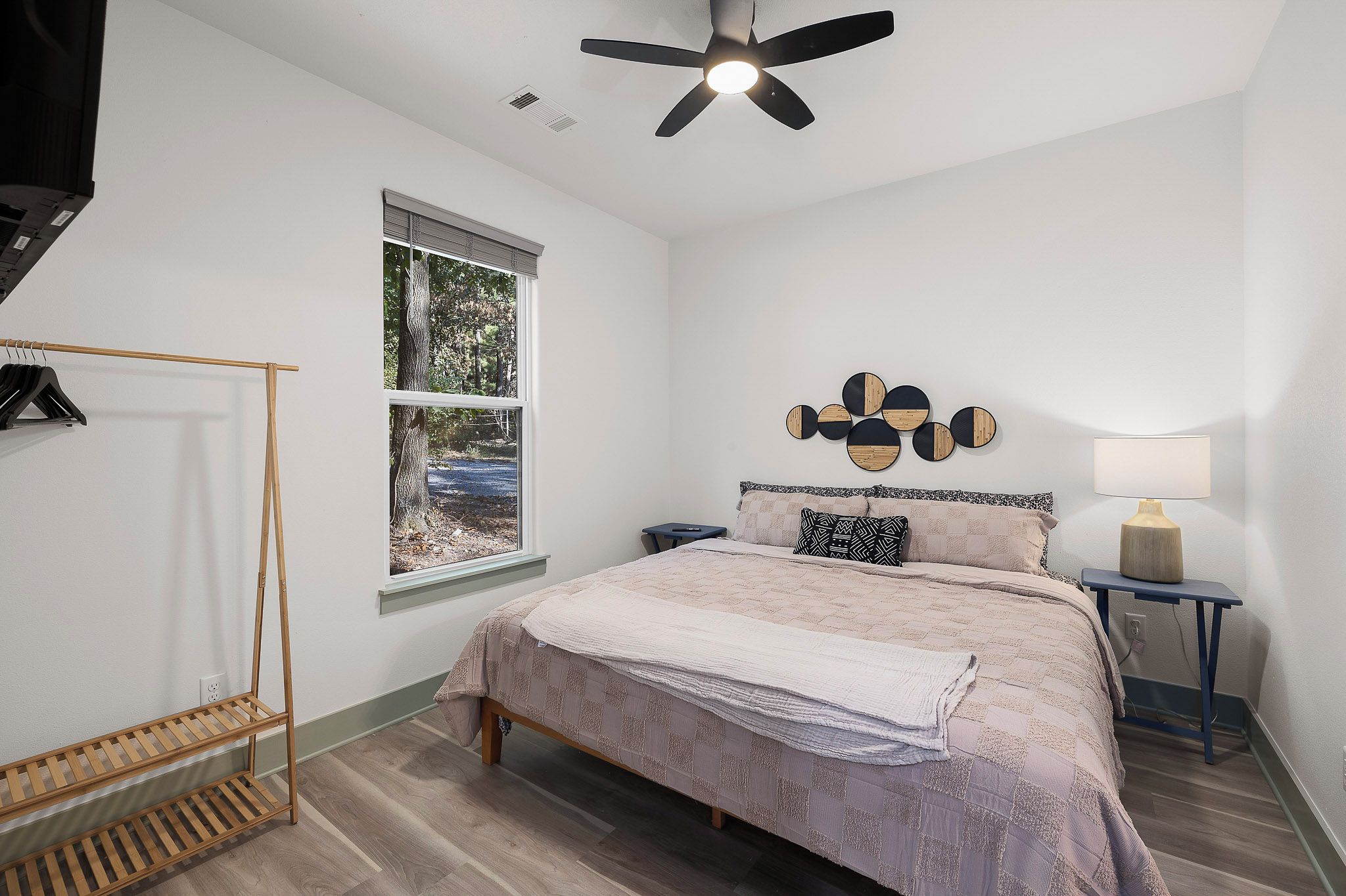 A bedroom with a bed, a window, a ceiling fan, a bedside table, and a wall-mounted lamp.