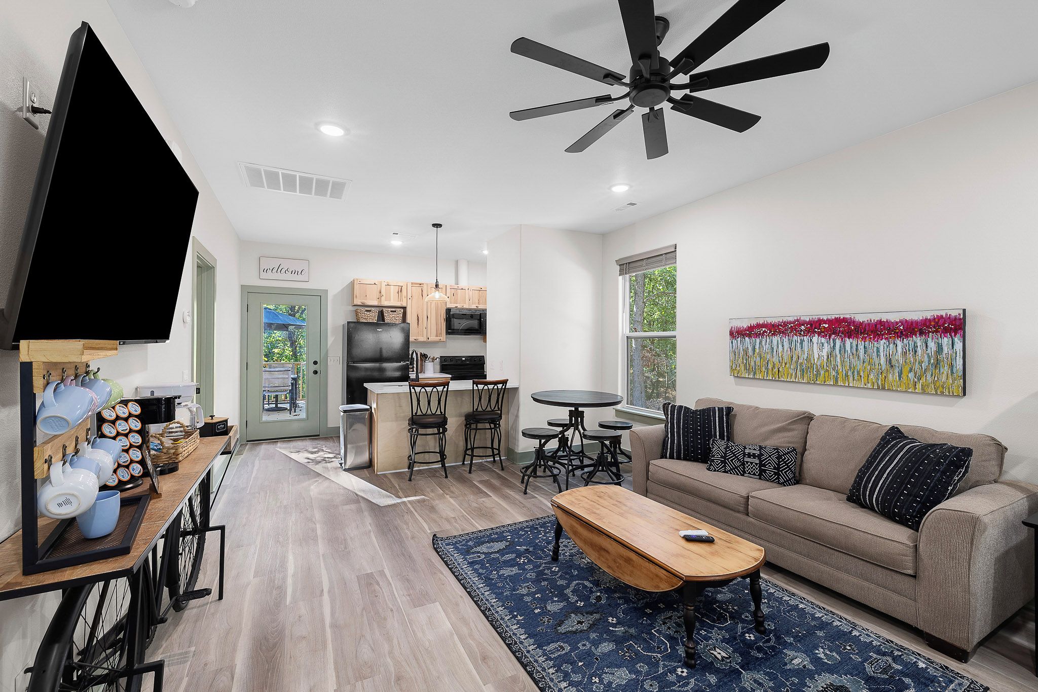 A modern living room with a sofa, coffee table, and a TV. There's a kitchen area with cabinets and a dining table.