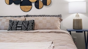 A bedroom with a bed, pillows, a wall-mounted light fixture, and a bedside table.