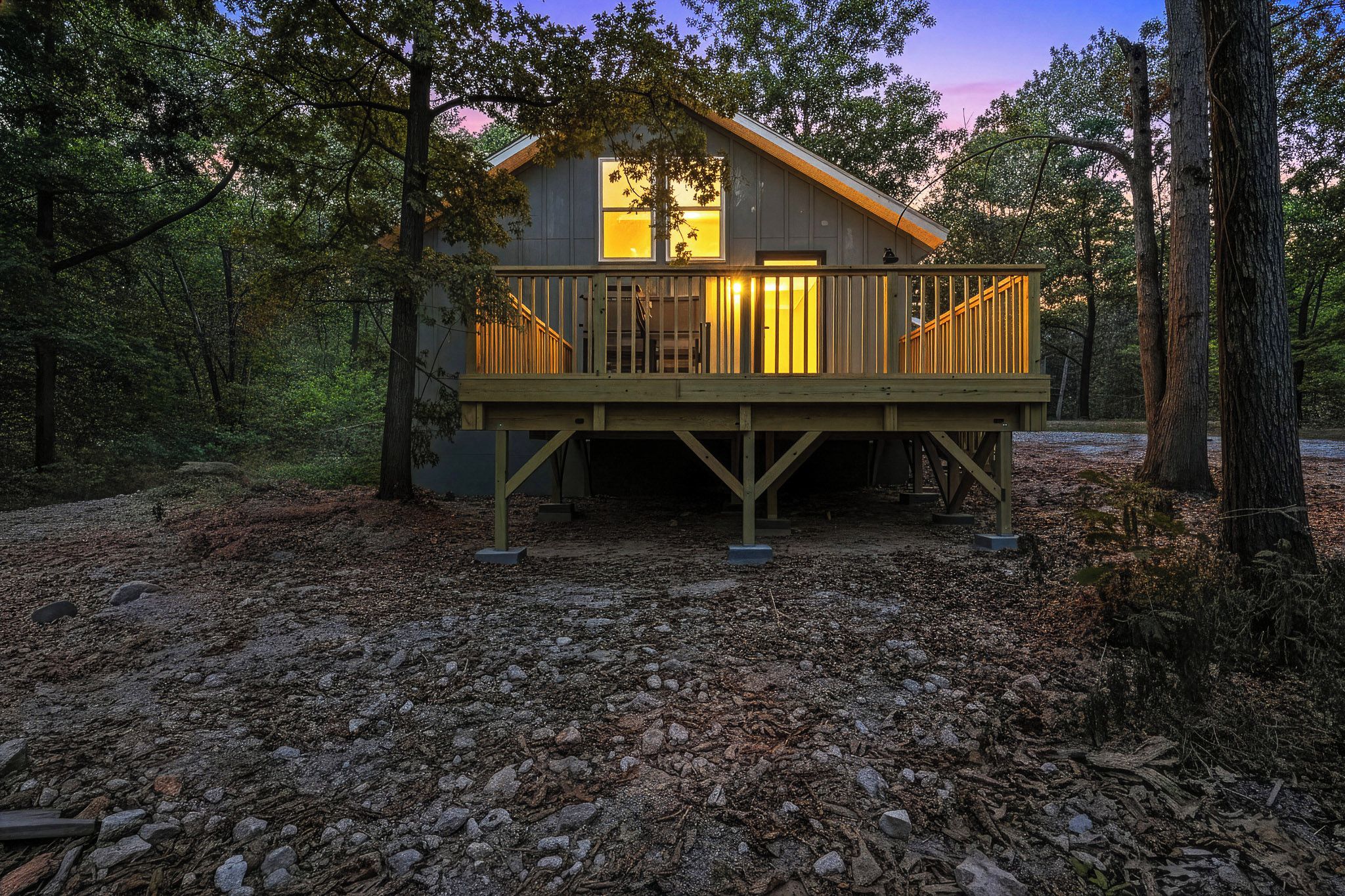 Eine Holzhütte mit einer Holzterrasse, umgeben von Bäumen und einem von Laub bedeckten Waldboden.