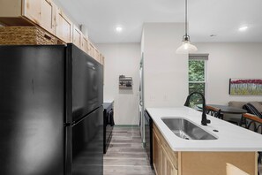 A modern kitchen with a black refrigerator, a stainless steel sink, and wooden cabinets. - Lovely 2-bedroom 2 bath brand new home on 5 acres just outside of town (Gravette)