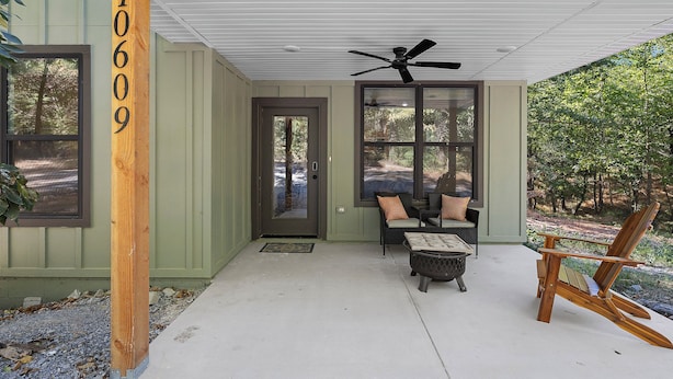 A covered porch with a ceiling fan, a door, and a seating area with cushions.