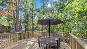 A wooden deck with a table and chairs, surrounded by a wooden railing, set in a wooded area.