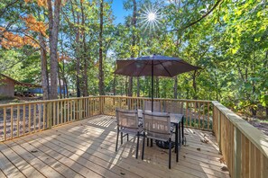 Eine Holzterrasse mit Tisch und Stühlen, umgeben von einem Geländer, in einem bewaldeten Gebiet.
