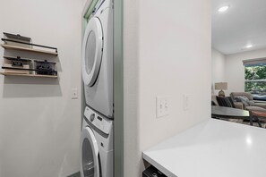 A laundry room with stacked washers and dryers, a table, and a window with a view of trees.