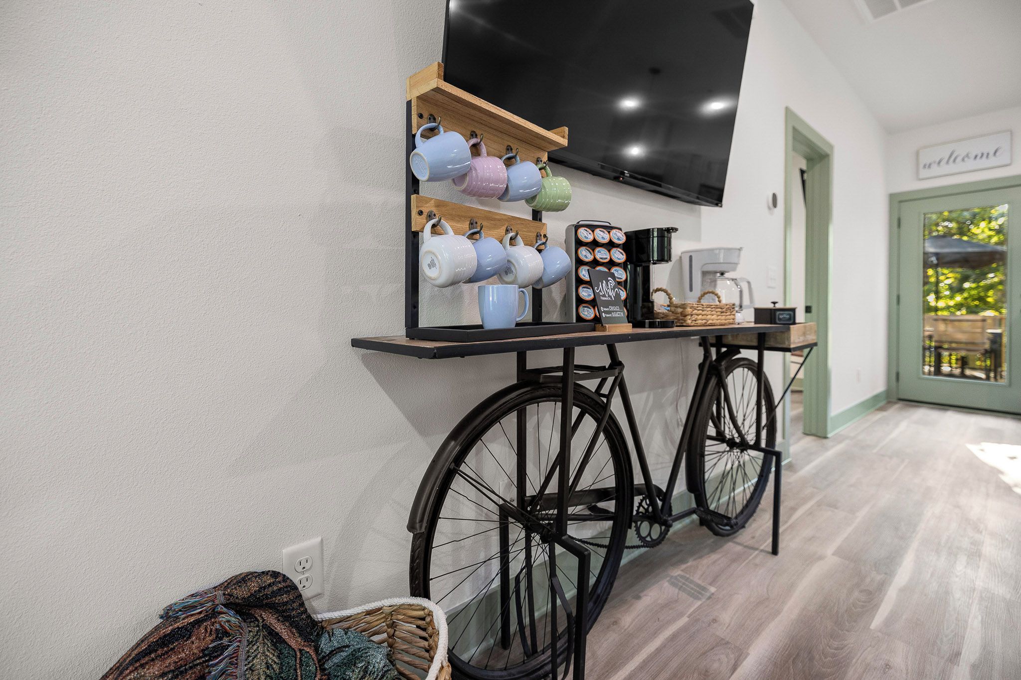 Une pièce équipée d’un vélo d’appartement, d’un coin café avec des tasses et une machine à café, et d’un téléviseur fixé au mur.
